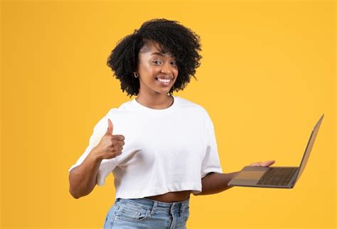 Cheerful young black curly lady in white tshirt show thumb up laptop ...