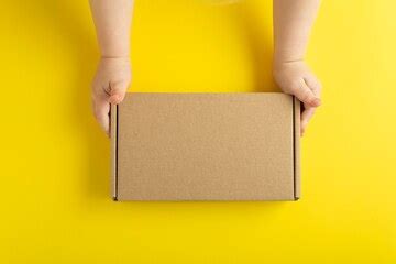Cardboard box in small childrens hands. yellow background, top view ...
