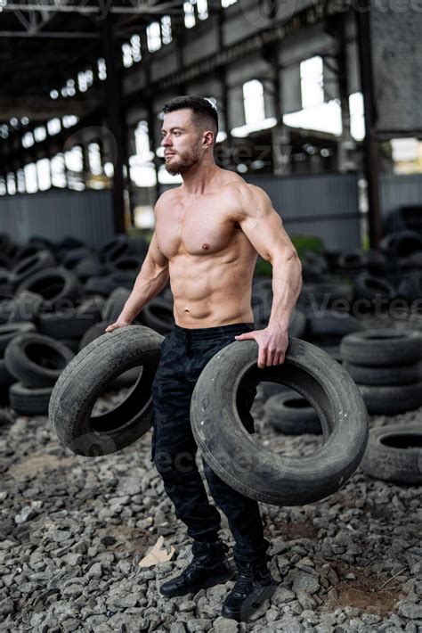Strong young man lifts tires shirtless. Big muscles and perfect abs ...