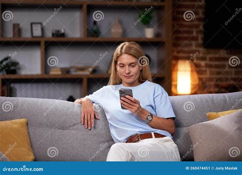 Blonde Girl Sitting on the Couch Looks into the Smartphone, Chatting ...