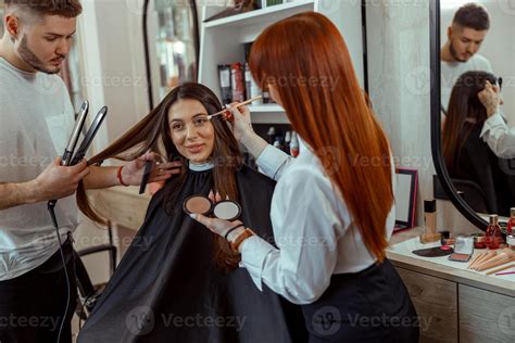 Professional makeup artist and hairstylist preparing female customer in ...