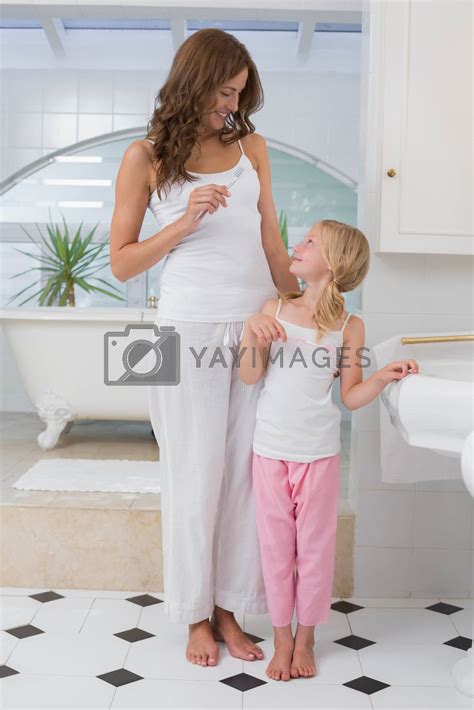 Girl brushing teeth as she looks at her mother in bathroom by ...