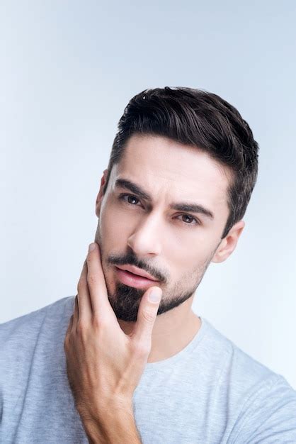 Portrait of a young man in gray t-shirt posing against a white wall ...