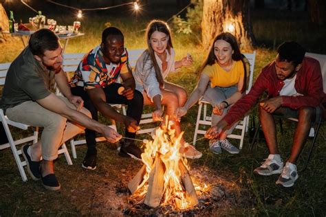 Group of multiracial restful friends roasting marshmallows while ...
