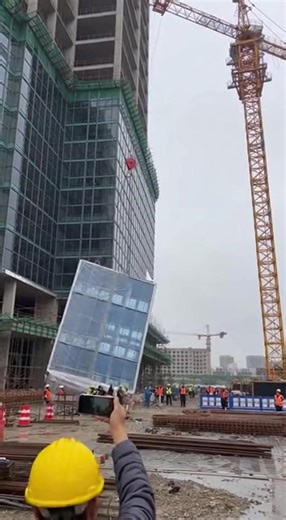 CRANE LOAD SNAPS OFF HIGH-RISE, SLAMMING INTO BUILDING AND CAUSING TOWER CRANE TO TOPPLE December 15, 2025 – Shenzhen, China A terrifying construction disaster unfolded at a high-rise building site when a massive glass curtain-wall section being hoisted by a tower crane broke loose, violently smashed into the structure, and triggered the crane itself to collapse in a catastrophic chain reaction. The entire event was captured on video by workers on the ground. The clip opens with dozens of crew m