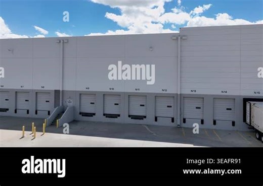 Orbit moving right to left around commercial warehouse loading dock with multiple industrial bay doors & visible shipping container. Industrial architecture ideal for logistics, freight, supply chain, warehousing, and commercial real estate concepts Stock Video Footage - Alamy