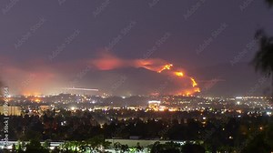 Timelapse forest fire on mountain range of residential neighborhood at night has planes dump water and smoke spreads.