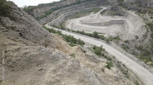 This 4K aerial video showcases a limestone quarry from a birds eye view, providing a comprehensive overview of the industrial mining site. The quarry is characterized by its vast, open-pit structure