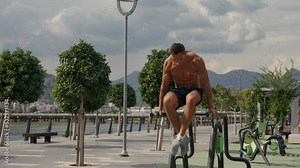 Man flexing abs on parallel bars in gym. Working on his core. Full length shot of a handsome and muscular young man working out on a dip bar outdoor