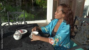 Asian woman is sitting on black iron table and drinking tea on a terrace, enjoy morning fresh air with view