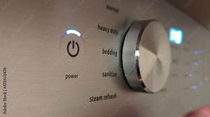 Male hand powering on and changing settings on a high-tech energy efficient washing machine appliance.