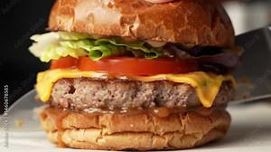 Footage of a gourmet burger being stacked layer by layer – bun, lettuce, juicy patty, cheese, tomato, and sauce – then cut in half to reveal the inside
