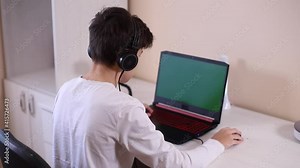 Teenage boy playing game on his pc computer in white room. Gamer capture video on web camera on laptop and phone on tripod
