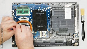 Repairman unscrews fan from laptop. Close-up. A repair technician disassembles a computer. Complicated electronics repair. Motherboard, processor, microchips and other computer parts in a workshop