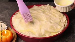 The filo dough pie is greased with butter for a crispy crust before baking in the oven