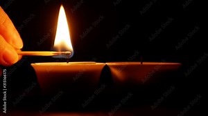 Hand lights a candle with a match in the dark.