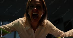 Portrait of angry business woman screaming at office desk late at night during thunderstorm. Emotions of fear of aggression and anger
