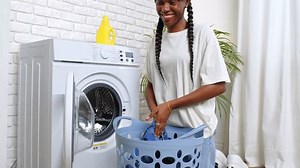 Woman Loading Laundry Into Washing Machine In Bathroom