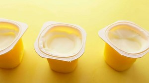 Fresh yogurt in a plastic container on yellow background