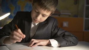 boy doing homework at home in the evening, sits at the table in a jacket