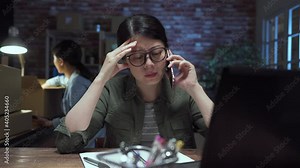 Angry businesswoman arguing talk on mobile phone in late night internet shop office. annoyed lady staff having conflict phone call conversation in office. two asian female coworkers in dark studio.