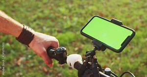 Close-up male cyclist using greenscreen mock-up smartphone tracking navigator on handlebar mountain bike in the park outdoors.
