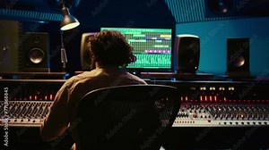 Tracking engineer processing and mixing sound on audio console with moving faders and colored meters. Music producer working on a new album, creating a hit song in studio. Camera B.