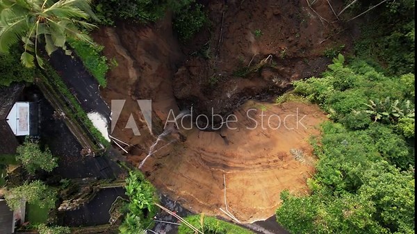 This detailed top-down view captures destruction caused by local landslide, which has completely destroyed part of countryside road. Aerial camera looks straight down and moves lower.