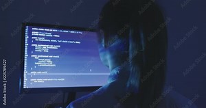 Experienced IT woman programmer works on a new program. Young woman hacker writes the source code of the software at dark room. Back view.