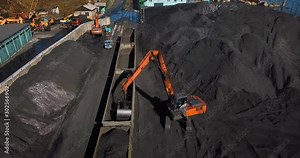 Coal port top view. Loading coal into railway wagons using an excavator. Stevedoring company.