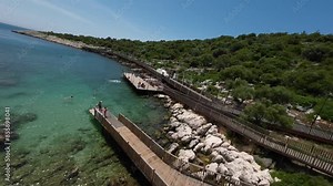 lively beach scene in Turkey with vacationers enjoying the clear turquoise waters and rocky coastline. Wooden walkways provide easy access to the water, perfect for relaxation and fun in the sun