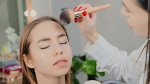 Artist expertly applies powder in sweeping motion on lady face. Skilled woman ensures even and smooth coverage enhancing young female features