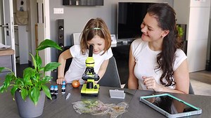 Little girl and her mother examining onion skin under a microscope at home. Concept of family science education and early biology learning. High quality 4k footage