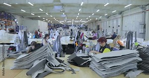 Many seamstresses work in a garment factory. Working process at a garment factory. Large sewing workshop. Seamstresses make products in a factory. Garment factory