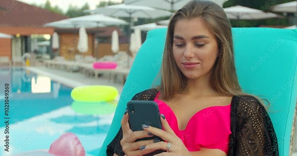 Summer girl using smartphone and sunbathing at swimming pool. Female model relaxing outdoors at sunny day. Stock Video