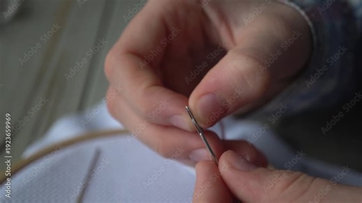 The hands of a child insert a floss thread into a sewing needle, the girl is preparing to embroider.