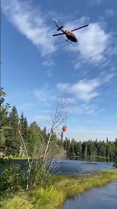 Helicopter dips bambi bucket in Mile 81 Pond along the Alaska Highway - Pogo Mine Road Fire 2023