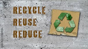 Animated recycle symbol made of recycled materials on cardboard square with reuse, recycle and reduce text on old wall