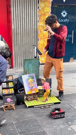 Indian Art Gallery on Instagram: "Meet @galeria_morionet bringing his tiny painter to life with incredible detail and charm 🎨 His marionette creates a whole world on a miniature canvas while crowds gather to watch the magic unfold 🌟 A beautiful reminder of how creativity can surprise us in the most unexpected corners of a city 🎭 Somewhere in the streets of Europe a puppeteer guides a quirky green pianist who plays with unbelievable expression 🎹 People stop in their tracks as the puppet’s tin