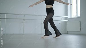 Fit girl in black clothes performing contemporary. Female dancer shows flowing motions, body and hands waves at white room. Modern ballet dance choreography. Young woman is moving smoothly