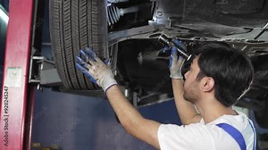 Auto mechanic using flashlight checking at the car tyre wheel during repairing at motor garage. After service concept