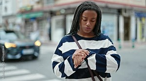 African american woman looking at the watch waiting with serious expression at street