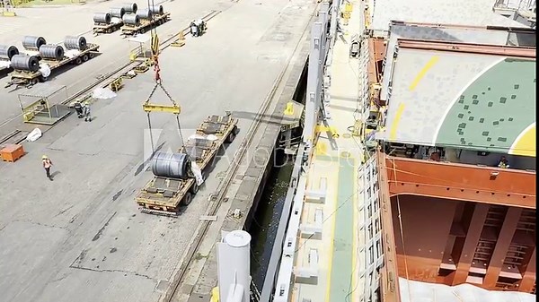 Real video of steel coil loading from the port quay onto a cargo ship using a ship crane. Heavy cargo handling, steel industry logistics, maritime transport, port and commercial freight operations