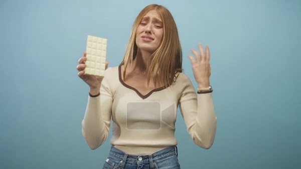 Young redhead woman holding a large white chocolate bar with hand raised and fingers splayed while grimacing in a studio setting; disgust doubt reluctance Stock Video Footage - Alamy