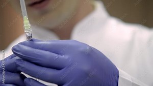 A cosmetologist’s hands in purple rubber gloves holding syringe with a needle for rejuvenating facial injections.