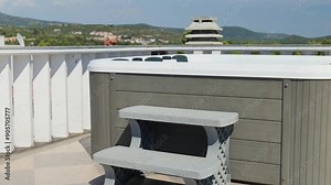 Outdoor hot tub on sunny rooftop deck with bubbling water and comfortable seating with beautiful view on touristic cityscape. Place for relaxation and leisure during summer vacations