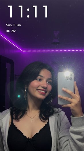 Aparnaahh on Instagram: "11.11♑🐐 ° Prompt ⬇️ Mirror selfie of a woman in her early 17s with I phone 16 pro Max[reference face from the photo] inside a room with purple LED strip lights on the ceiling. The woman is wearing a black Y2K bra ruffle top,and a grey colour zip open hoodie has a wolf cut hair with glossy red lips,gold geometic hoops,pink dewy blush.she is also wearing a cross artificial jewellery necklace. One hand is holding a phone with the flash shining brightly, held slightly away