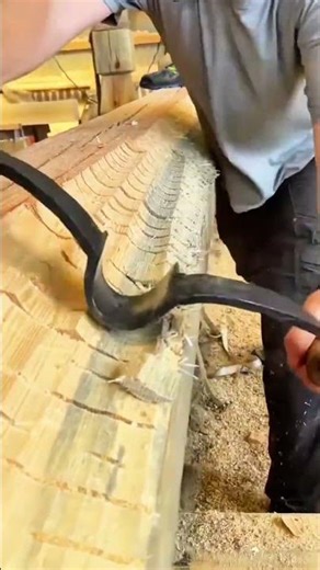 using a curved draw knife to smooth the surface of a large wooden log with a textured pattern