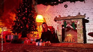 Woman lays out packed boxes of gifts under a Christmas tree while sitting on floor at night. A caucasian woman prepares for spending New Year at home. Theme of celebrating winter holidays