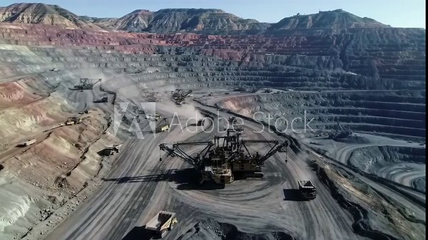 Heavy machinery operates in a vast open-pit excavation under a clear sky.